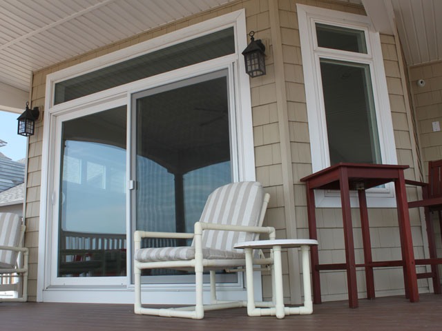 Tan siding exterior view of a porch with a new white trimmed screen door and window.