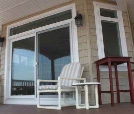 Tan siding exterior view of a porch with a new white trimmed screen door and window.